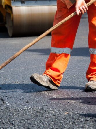 Operario trabajando en la imprimación y pavimentación de la Ruta Provincial 43. La obra, clave para la logística del litio, requiere especificaciones técnicas de alta resistencia para soportar el tránsito pesado y las amplitudes térmicas extremas de Antofagasta de la Sierra.