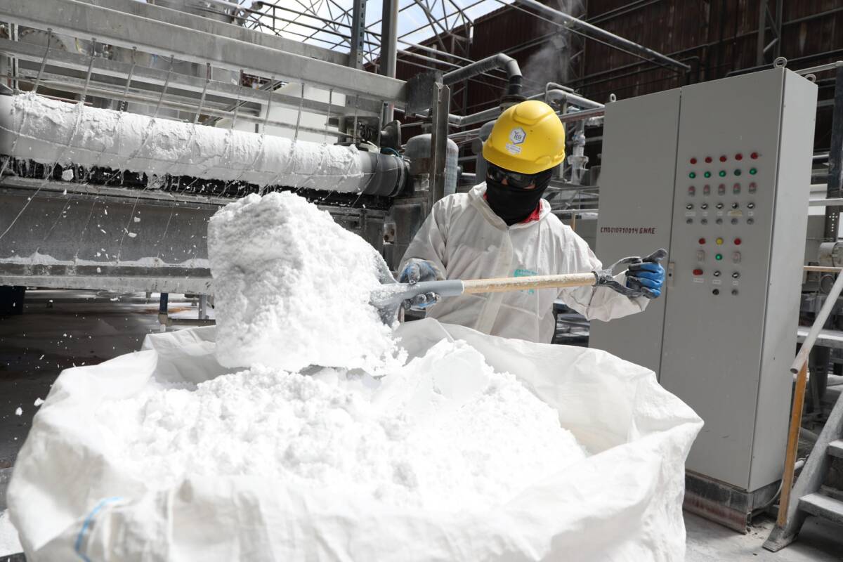 Operario en una planta industrial manipulando material blanco vinculado a la producción de litio, una actividad clave en el mapa minero en América Latina.