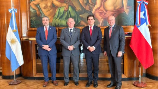 Cuatro representantes institucionales posan entre las banderas de Argentina y Chile durante una reunión vinculada al acuerdo para impulsar nuevos proyectos mineros.
