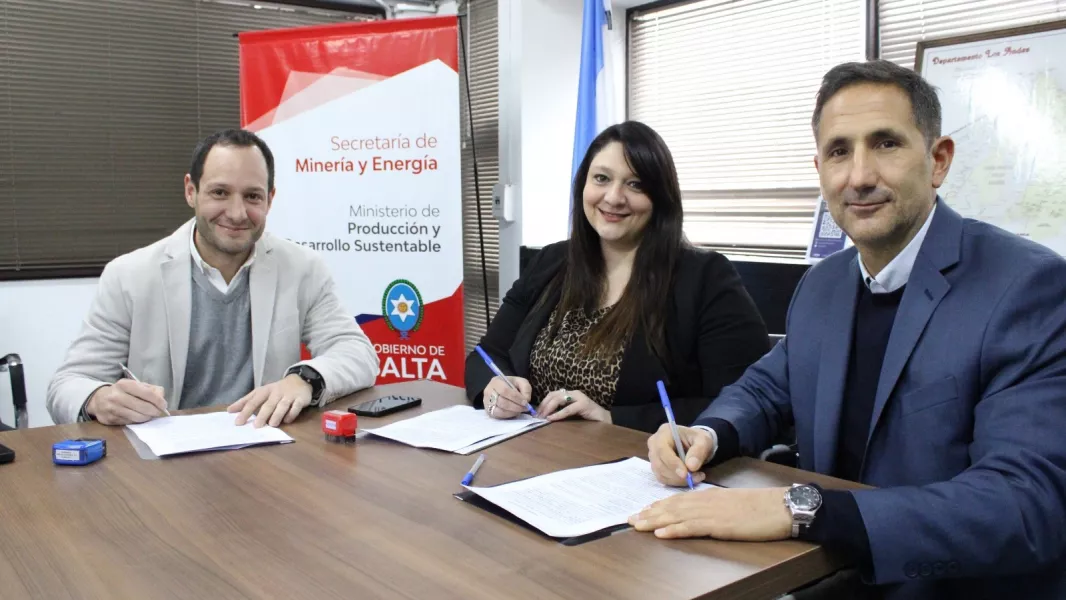 Tres personas firman documentos alrededor de una mesa, junto a un cartel de la Secretaría de Minería y Energía de Salta, en un encuentro sobre proveedores mineros.