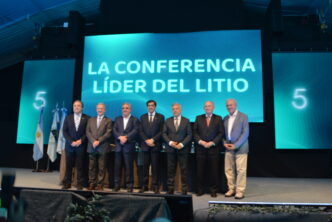 Siete participantes posan en el escenario de Litio en Sudamérica 2026, junto a banderas y una pantalla con la frase «La conferencia líder del litio».