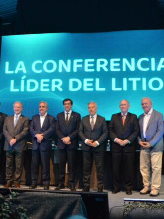 Siete participantes posan en el escenario de Litio en Sudamérica 2026, junto a banderas y una pantalla con la frase «La conferencia líder del litio».